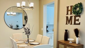 A dining area with a wooden table, white chairs, a chandelier, a round mirror, and a cabinet with a 'HOME' sign. - Meet. Play. Stay. • Relax & Play in Orlando (Orlando)