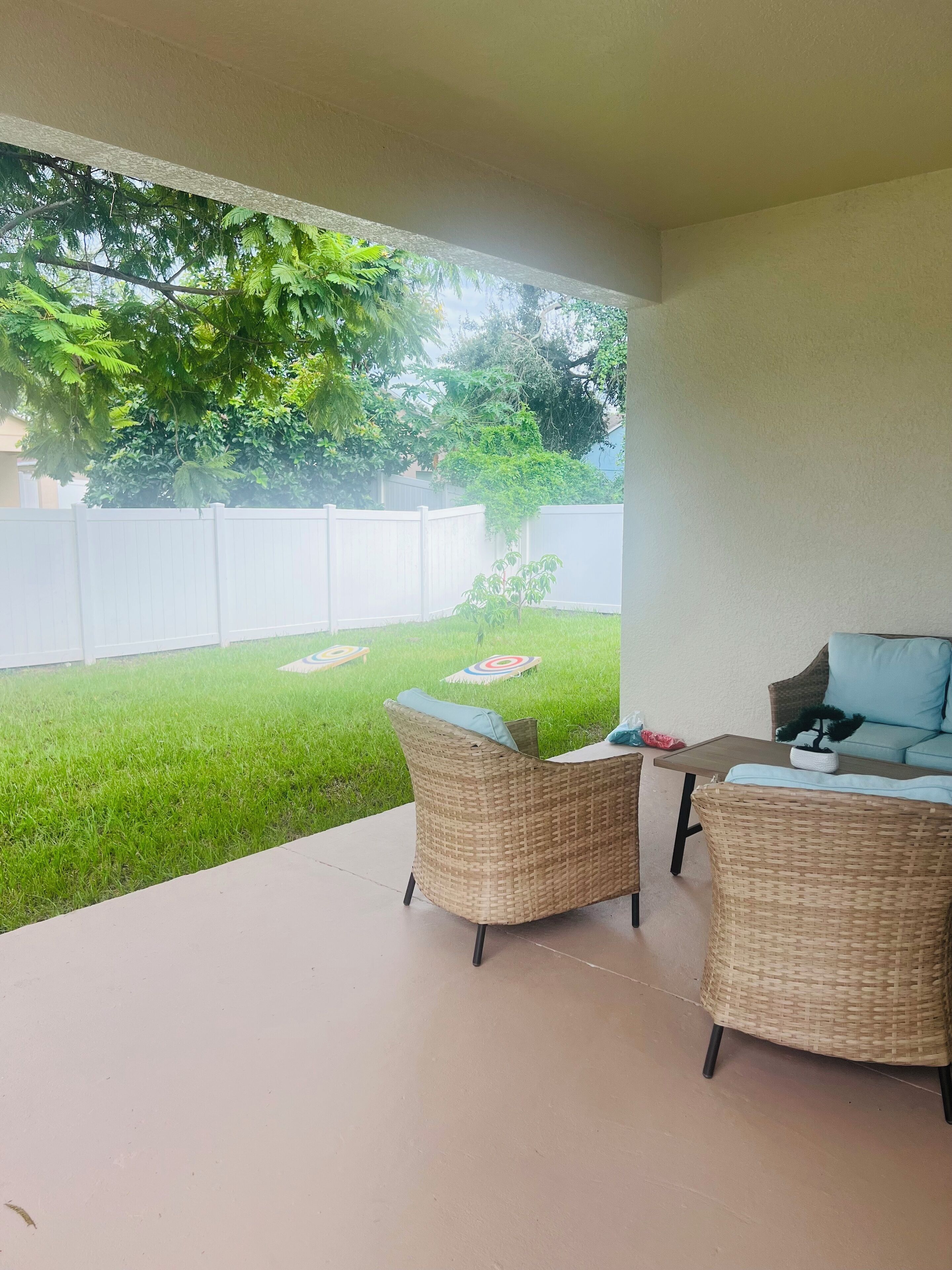 A covered patio area with wicker furniture and a view of a well-maintained lawn and white fence.