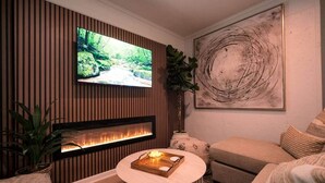 Un soggiorno moderno con camino, televisione montata su una parete rivestita in legno e un grande dipinto astratto.