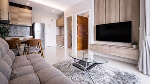 Ein modernes Wohnzimmer mit einer Couch, einem Esstisch, Stühlen, einem Glastisch, einem Flachbildfernseher und Holzschränken.