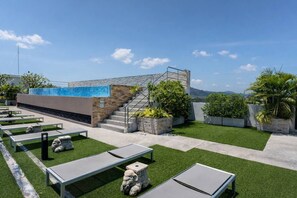 A rooftop terrace with artificial grass, outdoor seating, and a staircase leading to a building with a blue-tiled section. - Suite Solen 1br|pool View|rawai (Rawai)