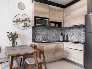A modern kitchen with wooden cabinets, a black countertop, a microwave, and a refrigerator. - Suite Solen 1BR|Pool View|Babylon Sky Garden Rawai (Rawai)