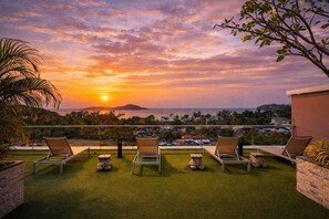 A terrace with lounge chairs, a view of the sunset over the sea, and a distant cityscape. - Suite Solen 1br|pool View|rawai (Rawai)