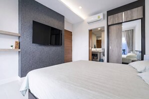 Ein modernes Hotelzimmer mit einem großen Bett, einem flachbildfernseher an der Wand und einem sichtbaren Badezimmer mit Spiegel und Waschbecken.