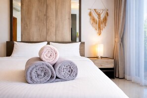 A neatly made bed with rolled towels, a bedside lamp, and a macrame wall hanging in a hotel room. - Suite Solen 1br|pool View|rawai (Rawai)