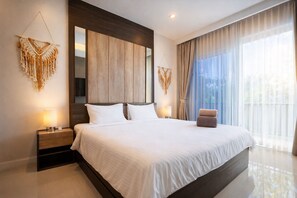 A modern hotel room with a large bed, two bedside tables, a large mirror, and a view of the outdoors through sheer curtains. - Suite Solen 1BR|Pool View|Babylon Sky Garden Rawai (Rawai)