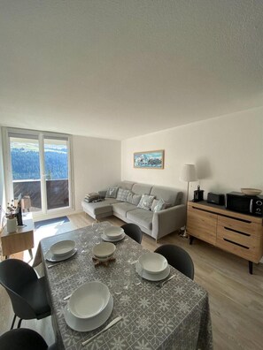 Un comedor con una mesa preparada para cuatro personas, un sofá gris, un armario de madera y un cuadro en la pared.