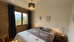 A bedroom with a bed, a desk, a window with curtains, a hanging light fixture, and two wall-mounted pictures. - 250m from ski slopes, 1st floor, view resort, terrace, parking, tv, ski locker, 53m², Les Saisies (Villard-sur-Doron)