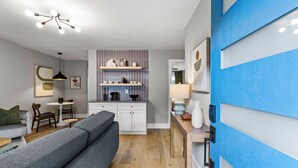 Ein modernes Wohnzimmer mit grauem Sofa, Holzboden und Küchenzeile mit weißen Schränken und einer blauen Akzentwand.