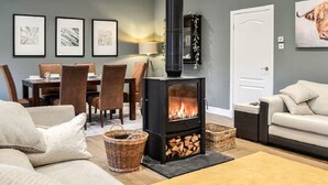 Un salon chaleureux avec un poêle à bois noir, un coin repas avec une table et des chaises, et un canapé.
