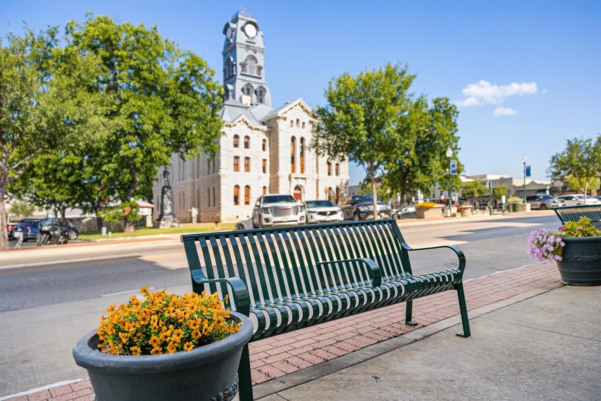 A bench with a flower pot on the sidewalk.