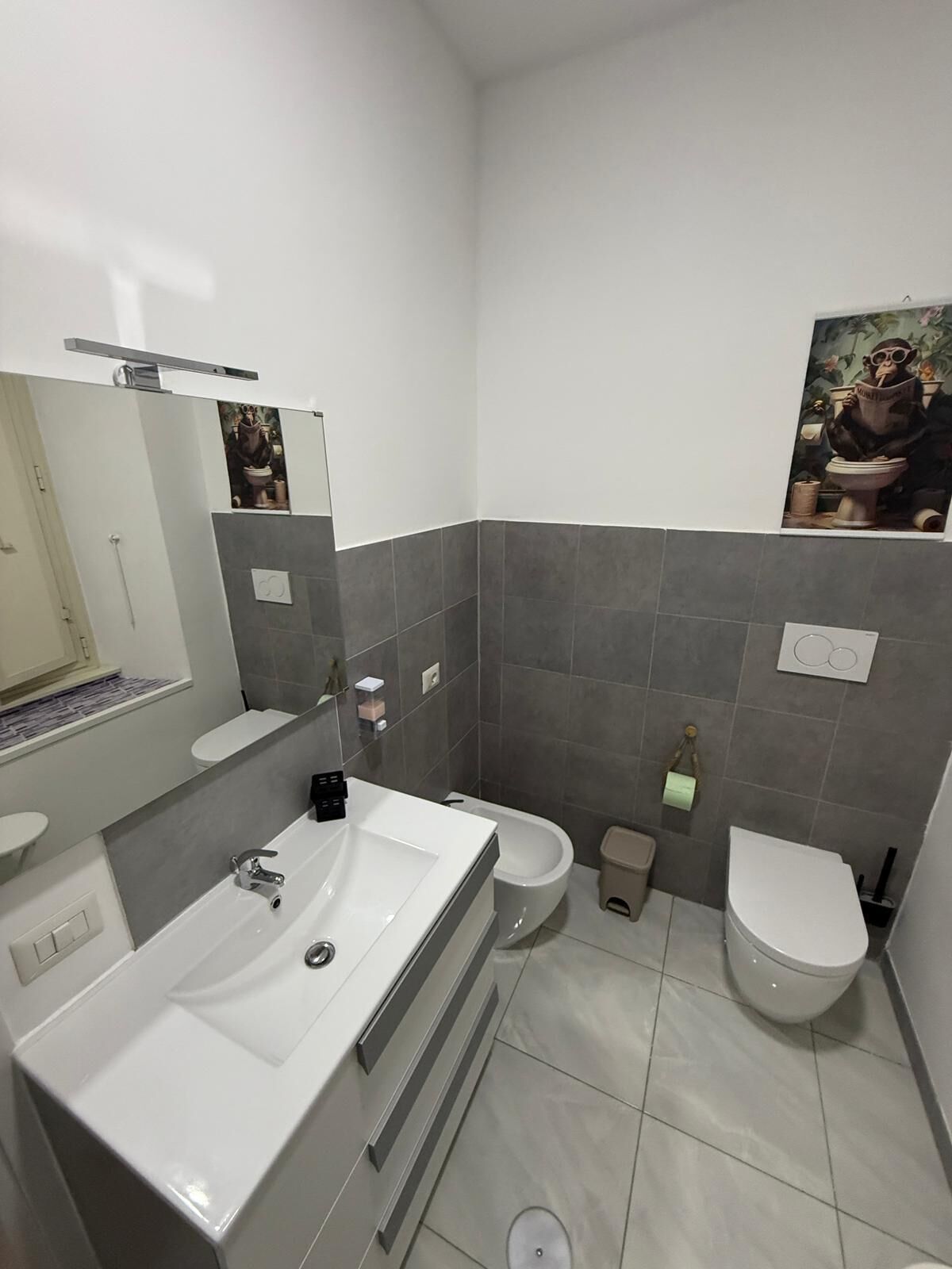 Een moderne badkamer met een groot wit wastafel, een spiegel, twee toiletten en een douchegedeelte.