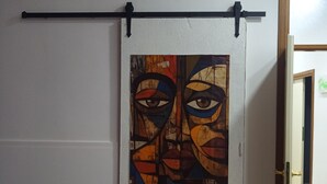 Une pièce dotée d’une porte coulissante, ornée d’un tableau abstrait aux couleurs vives, d’un climatiseur fixé au plafond et d’une poignée de porte bien visible.