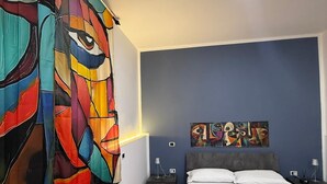 Une chambre avec une grande peinture abstraite sur le mur de gauche, un lit avec une literie rose et un mur d’accent bleu.
