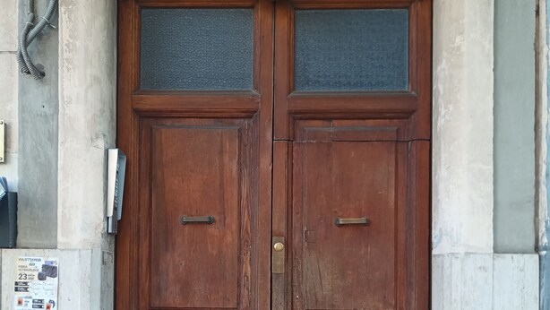 Une porte en bois à deux battants, dotée d’une poignée en métal et d’un panneau de verre au-dessus.