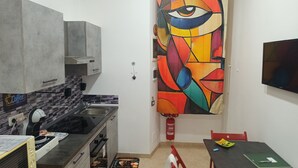 Une cuisine compacte au design moderne, équipée d’un four à micro-ondes, d’une cuisinière et d’un évier. Un tableau abstrait aux couleurs vives orne le mur, et un extincteur est fixé au mur.