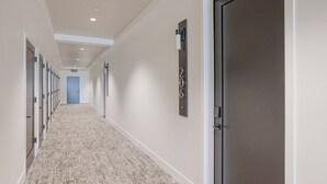 A hotel hallway with a carpeted floor, a blue door at the end, and a wall-mounted number plate. - Coastal Getaway with Ocean Views (Grover Beach)