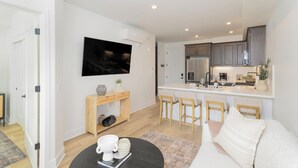 A modern kitchen with a central island, bar stools, and a flat-screen TV mounted above the island. - Coastal Getaway with Ocean Views (Grover Beach)