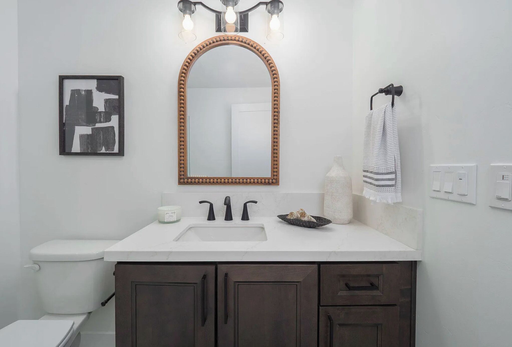 A bathroom with a white sink, dark wooden cabinets, a large mirror with a wooden frame, and a towel hanging on a hook.