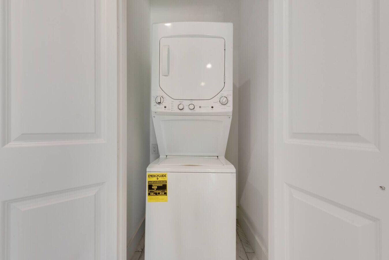 Una lavadora blanca en un pasillo estrecho con puertas blancas a cada lado.