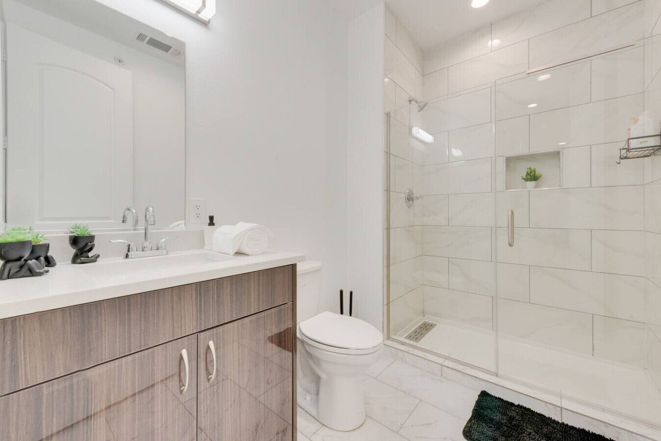 A modern bathroom with a wooden vanity, white sink, and a glass shower enclosure.