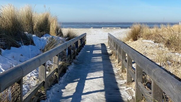 A wooden boardwalk leading to a beach with snow on the sides. - Ostfreesenstuuv max. 4 person in the heart of Neßmersiel Terrace, garden, WLAN- Wallbox (Nessmersiel)