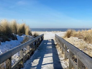A wooden boardwalk leading to a beach with snow on the sides. - Ostfreesenstuuv (max. 4 people) in the heart of Neßmersiel: Terrace, garden, Wi-Fi, charging station (Nessmersiel)