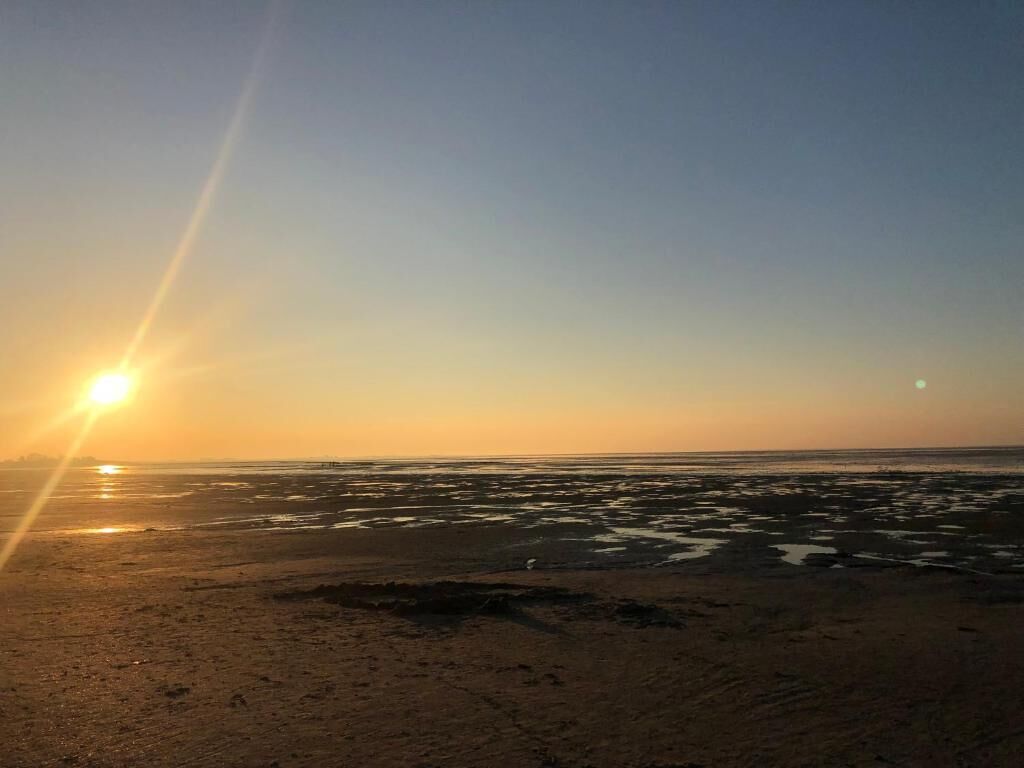 Uma praia ao pôr do sol, com o sol baixo no horizonte, refletindo na areia molhada.