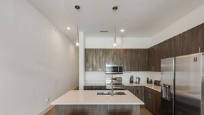 Uma cozinha moderna com armários de madeira escura, eletrodomésticos de aço inoxidável e uma ilha central com dois banquetas pretas.