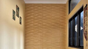 Una habitación con pared beige con textura, una pequeña mesa de madera, un tapete rojo estampado y una ventana con cortina decorativa.