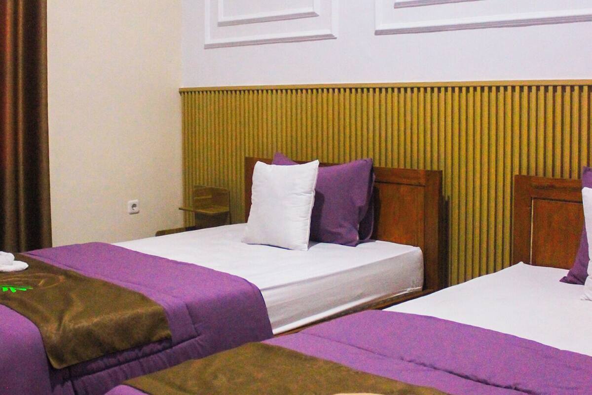 Habitación de hotel con dos camas, cada una con ropa de cama púrpura y cabecero marrón.