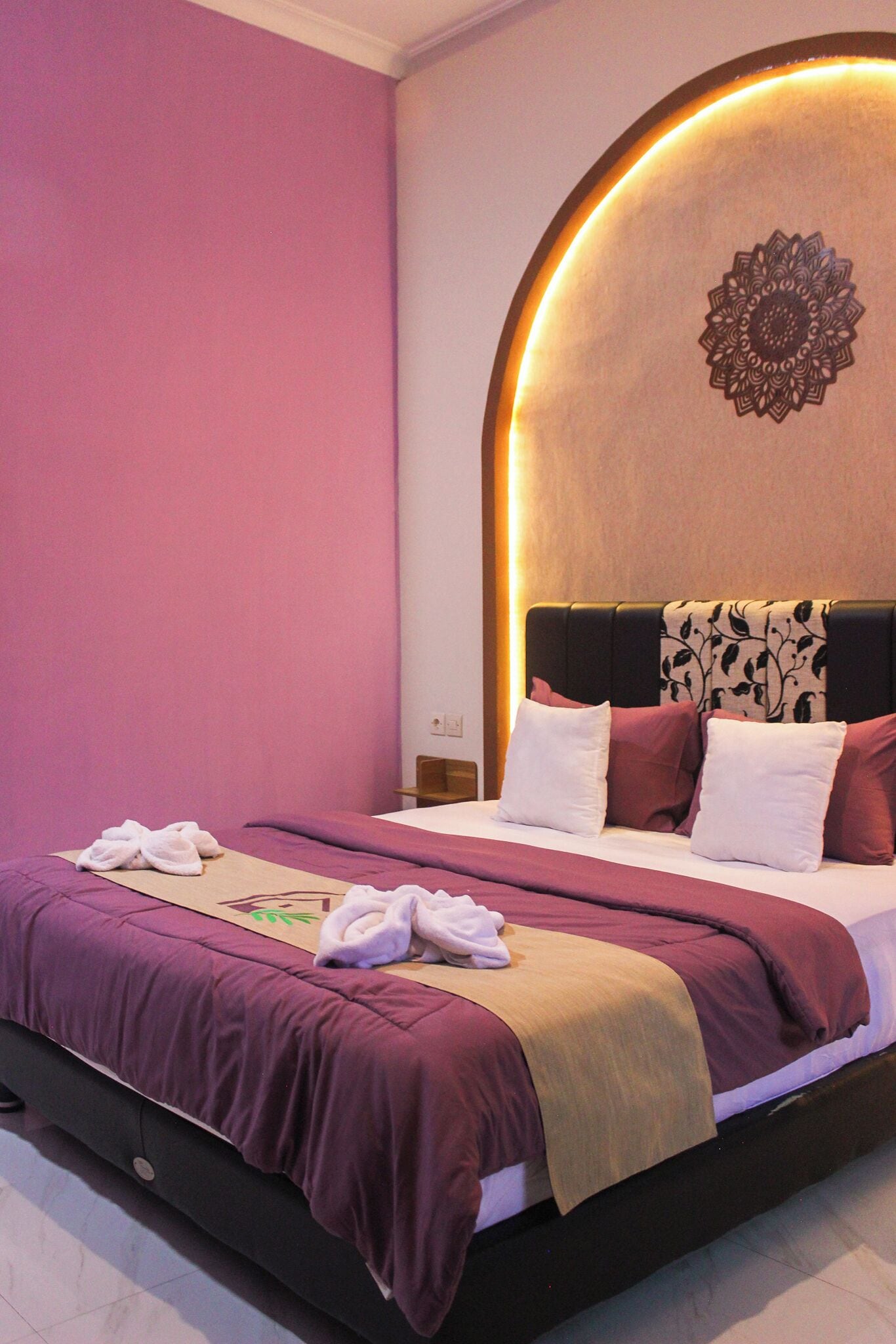 Una cama bien hecha con una colcha morada y beige, almohadas blancas y un cabecero decorativo con un diseño circular.
