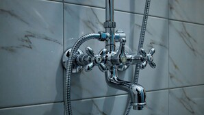A chrome showerhead with multiple nozzles and a flexible hose attached to a wall with marble tiles. - Gibson Motel (Mbarara)