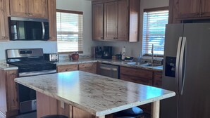 A modern kitchen with wooden cabinets, a stainless steel refrigerator, a built-in oven, and a large island with bar stools. - Wake up to breathtaking sunrise views from the porch of this 2 BR waterview home (Sturgeon Bay)