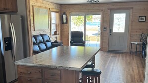 A spacious kitchen with wooden cabinets, a large island, and a refrigerator. - Wake up to breathtaking sunrise views from the porch of this 2 BR waterview home (Sturgeon Bay)