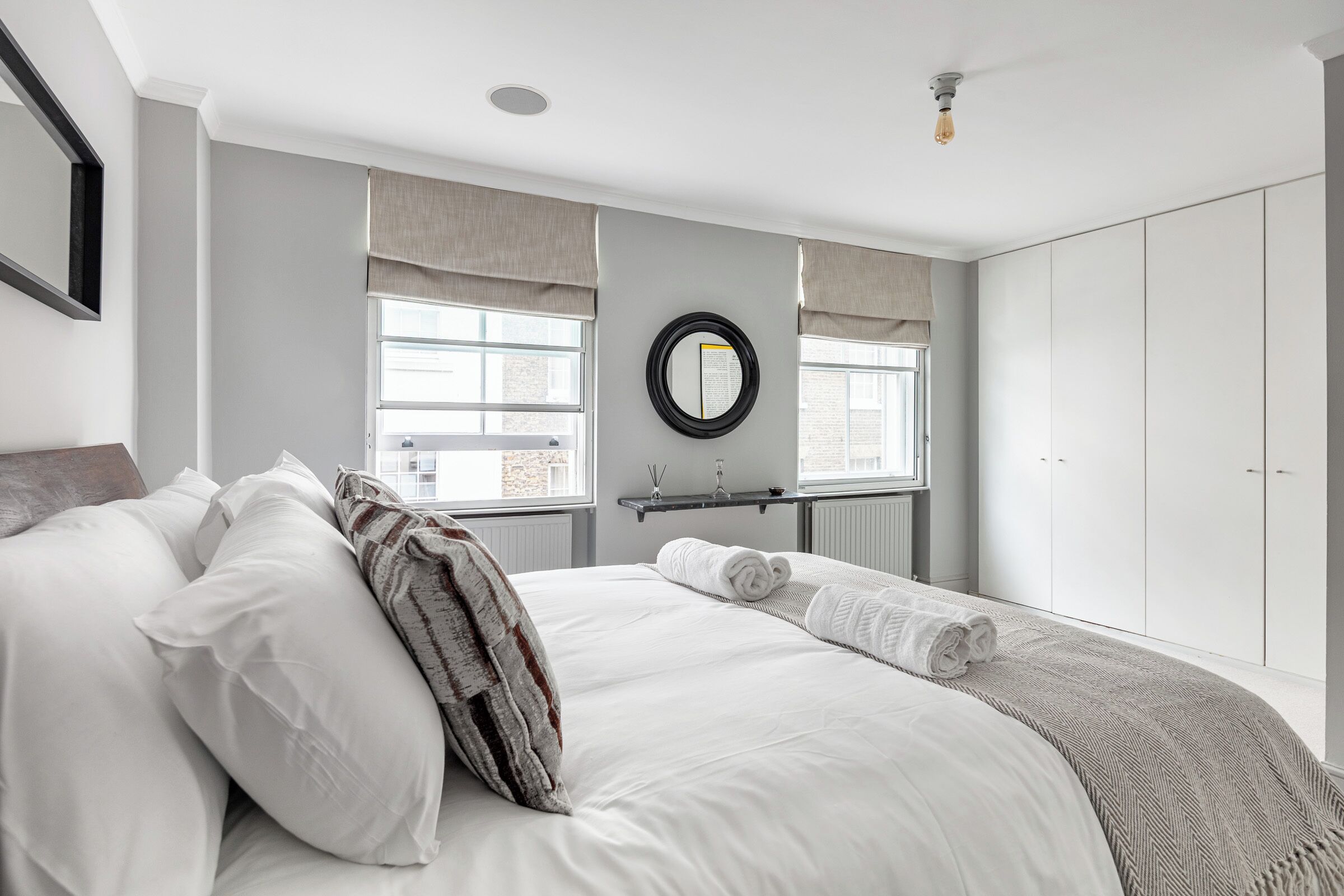 Une chambre à coucher moderne avec un grand lit, un miroir rond et une armoire.