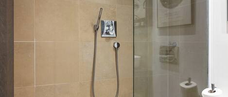 Een moderne badkamer met een douchecabine van glas, beige tegels, een toiletrolhouder en een lijst met een foto aan de muur.
