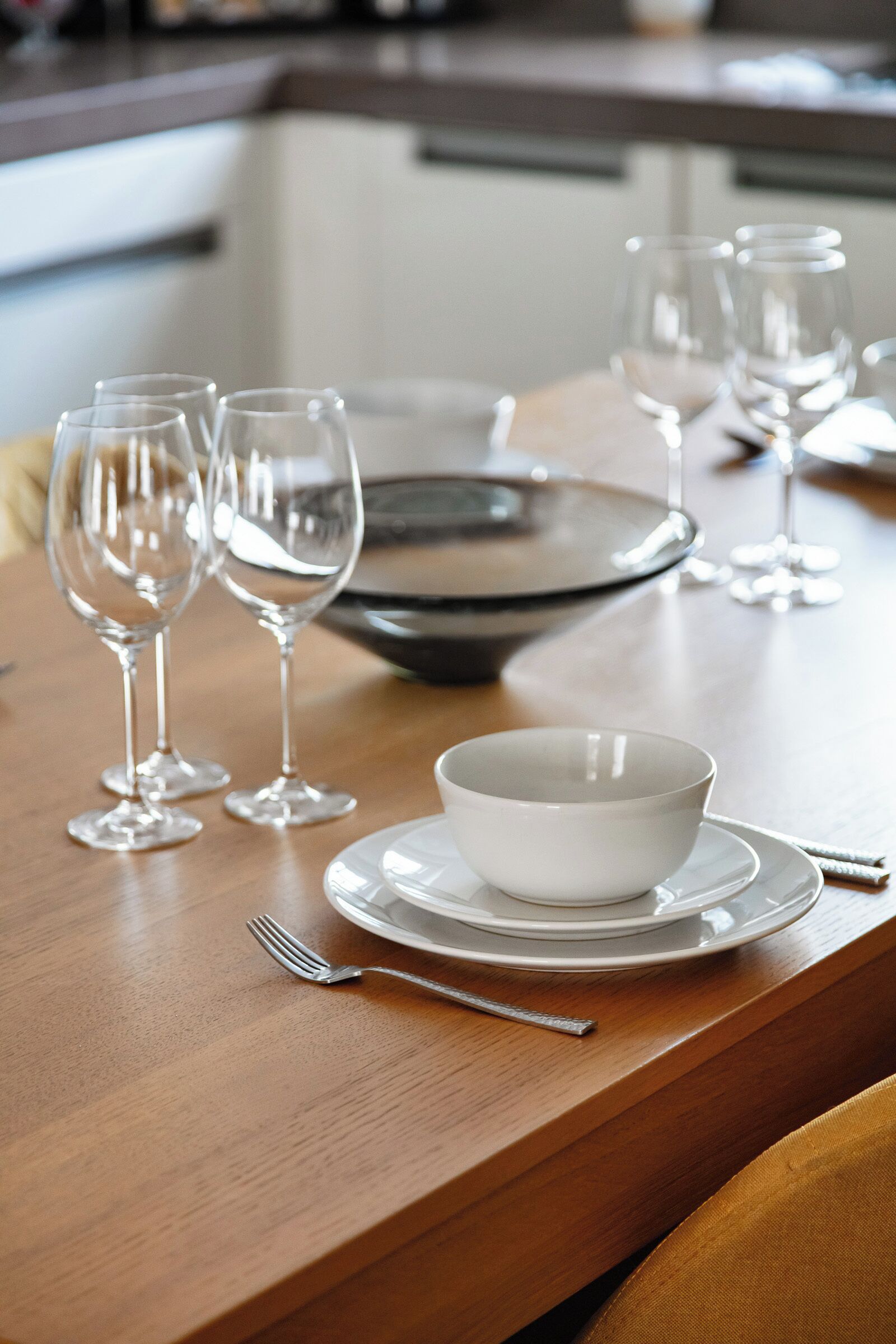 A dining table set with white plates, bowls, and wine glasses, with a fork and spoon on the table.