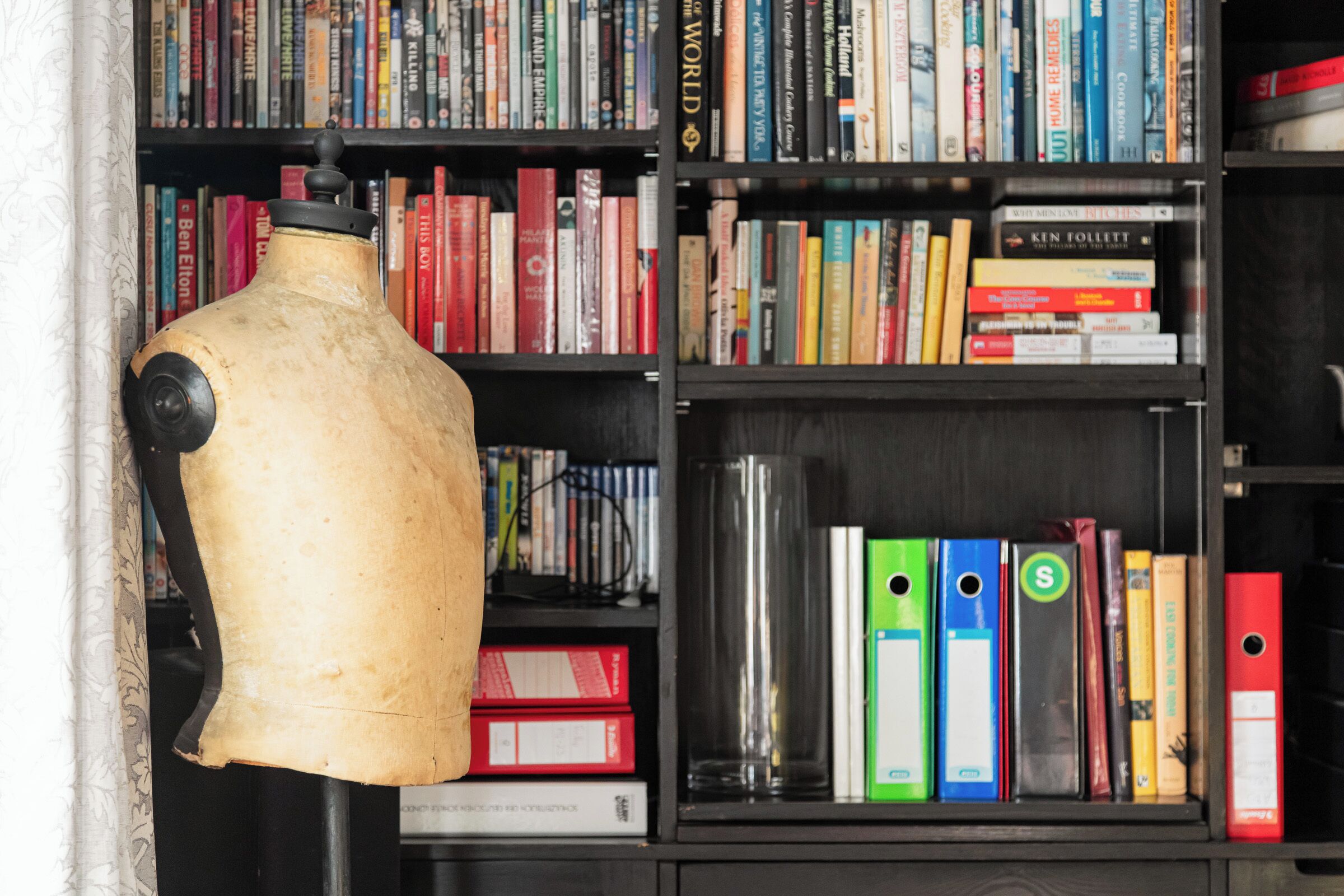 Un mannequin se tient devant une bibliothèque remplie de livres et de classeurs.