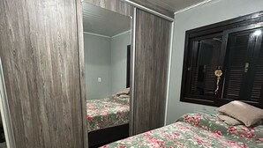 A bedroom with a wooden wardrobe, a bed with a floral bedspread, and a window with blinds. - Ape in the mountains (Caxias do Sul)