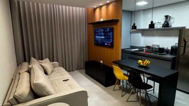 A modern living room with a sofa, a small round table, and a kitchen area with a dining table and chairs. - Ape in the mountains (Caxias do Sul)