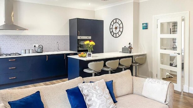 Een moderne keuken met een centraal eiland, een zithoek met stoelen en een bank met blauwe en witte kussens.