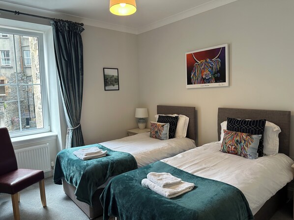 Een hotelkamer met twee bedden, een raam met gordijnen, een radiator, een stoel en kunst aan de muur.