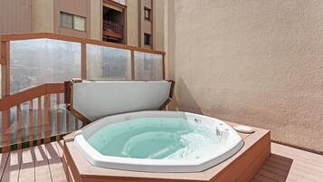 A hot tub on a wooden deck with a glass balustrade and a building in the background.