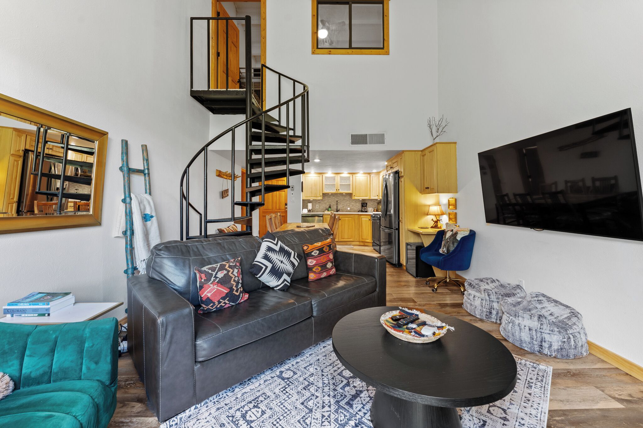 Una sala de estar moderna con un sofá de cuero negro, una mesa redonda para café y una escalera espiral que conduce a un nivel superior.
