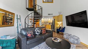 Una sala de estar moderna con un sofá de cuero negro, una mesa redonda para café y una escalera espiral que conduce a un nivel superior.
