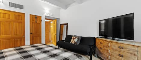 Ett sovrum med en säng, en soffa, en tv och en byrå i trä.