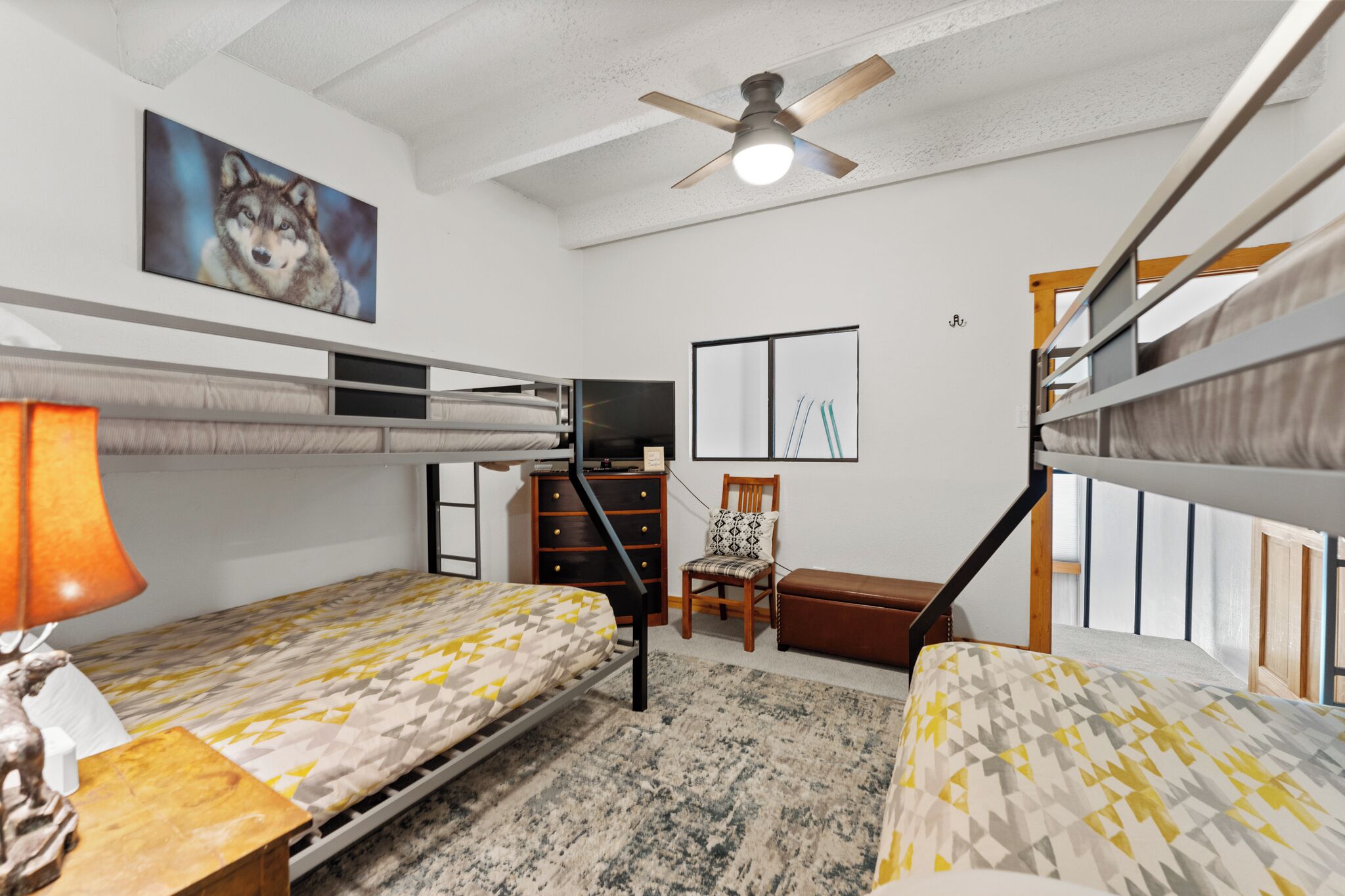 A bunk bed room with a ceiling fan, a desk with a lamp, a chair, and a painting of a wolf.