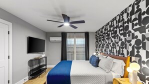 Un dormitorio moderno con cama, ventilador de techo, televisor y pared con diseño.