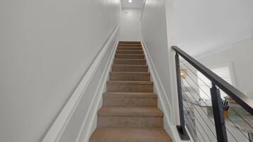 Un escalier dont les marches sont recouvertes de moquette, avec des murs blancs et une rampe noire.